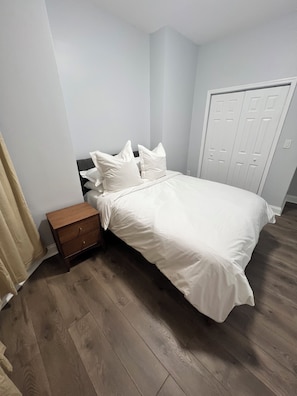 Una camera da letto con un letto, un comodino, una cassettiera in legno e una porta.