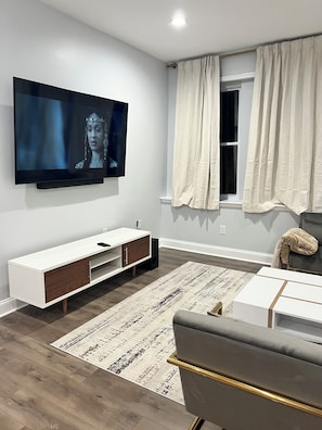 Ein modernes Wohnzimmer mit einem flachbildfernseher an der Wand, einer weißen Unterhaltungsecke, einem grauen Sofa und einem gemusterten Teppich.