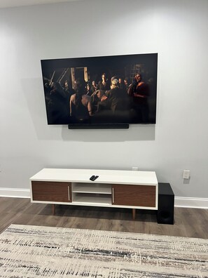 A flat-screen TV mounted on a wall above a white console with wooden accents and a remote control on it.