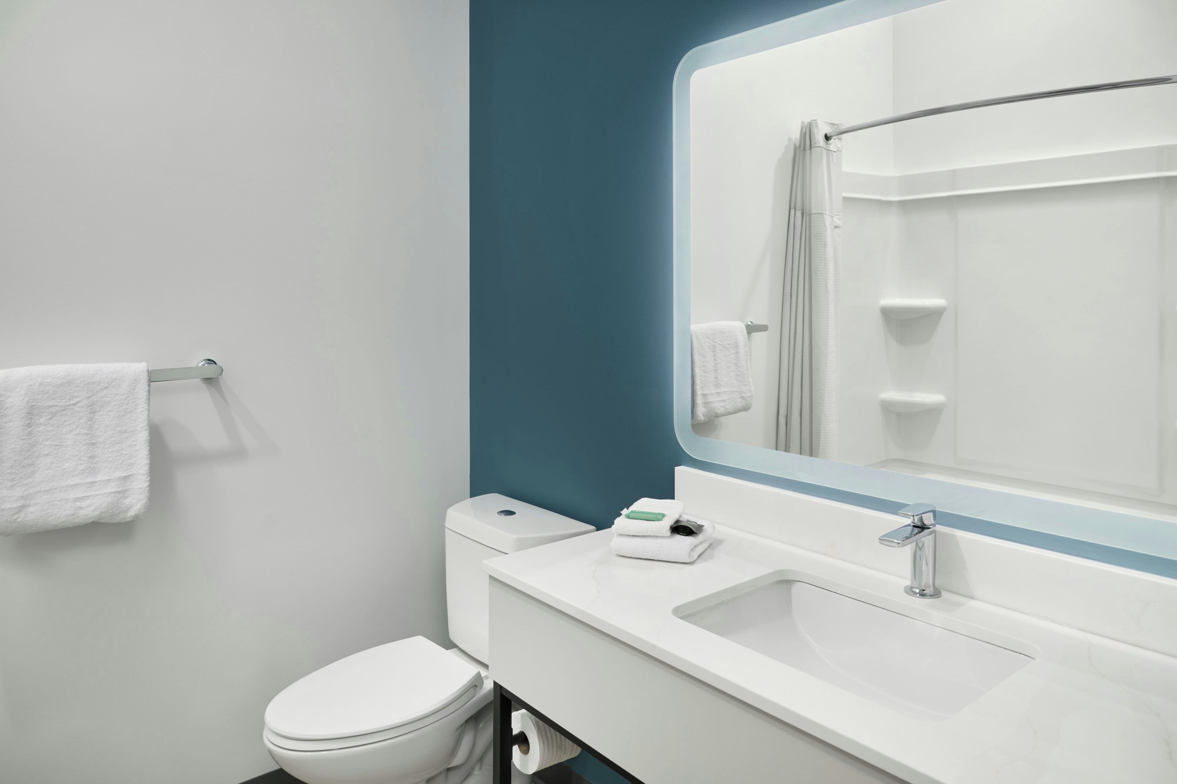 A modern bathroom with a toilet, sink, and a large mirror.