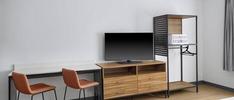 Una habitación de hotel moderna con un escritorio de madera, dos sillas, un televisor, un armario y una cama.