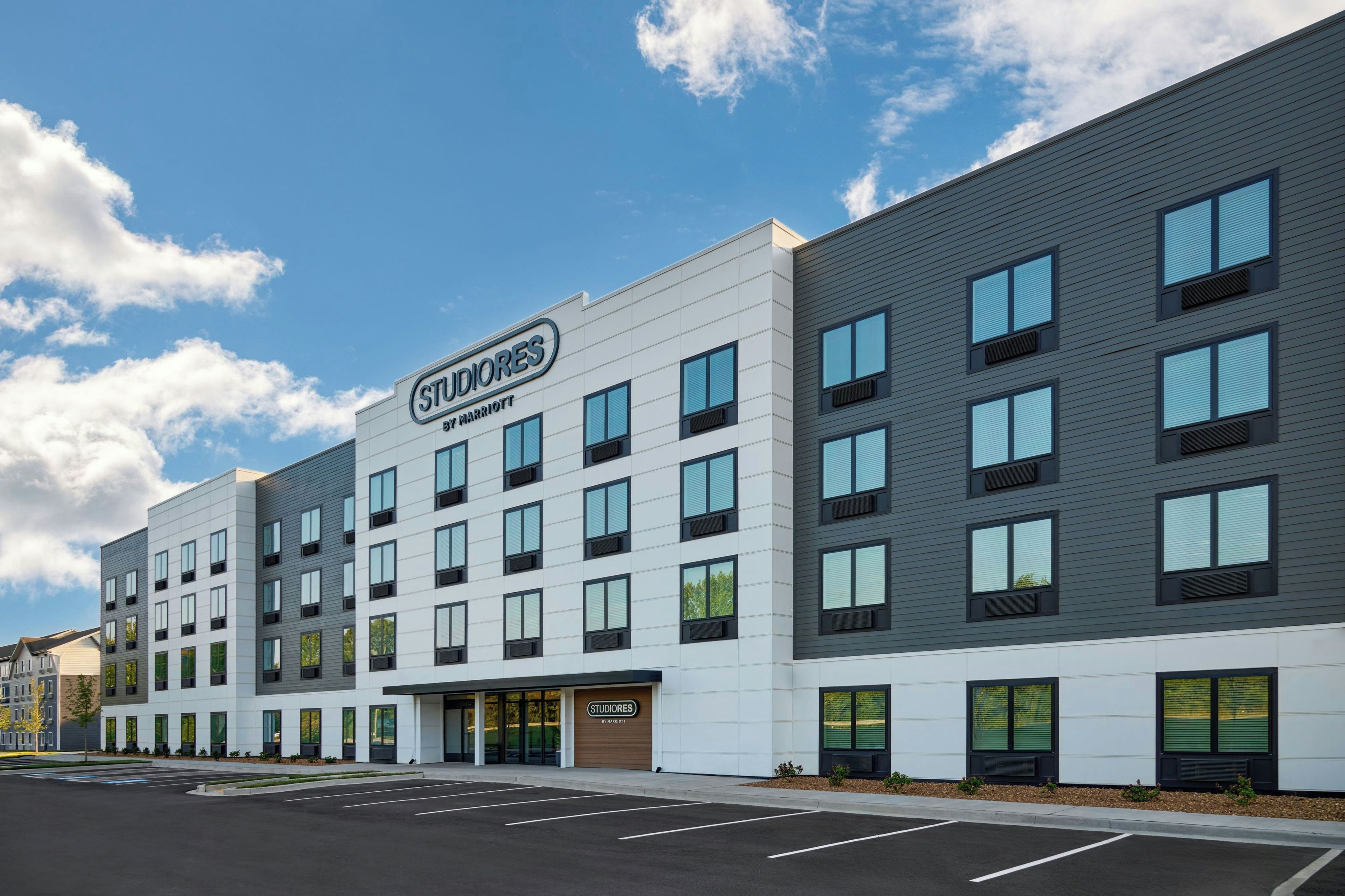 A modern hotel building with a sign reading 'STUDIORES BY MARRIOTT' and a parking lot in front.