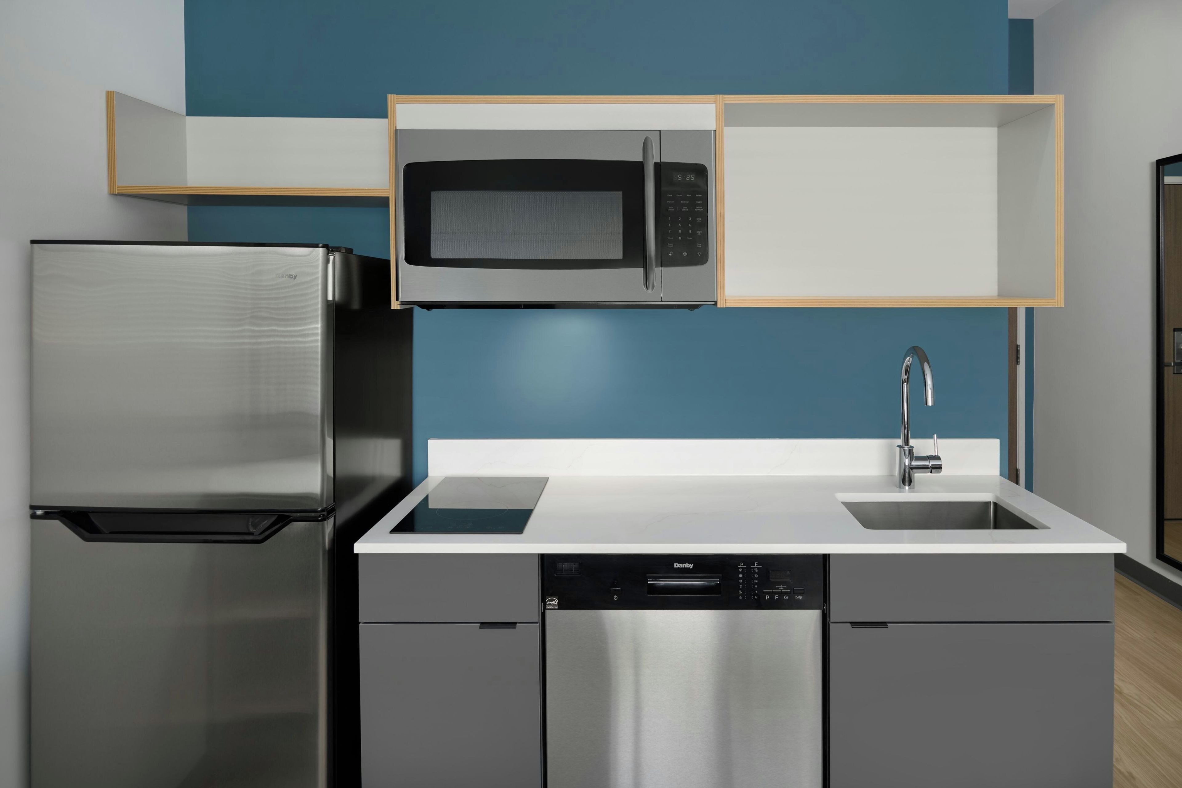 A compact kitchen with a stainless steel refrigerator, a microwave, a dishwasher, and a sink with a modern faucet.