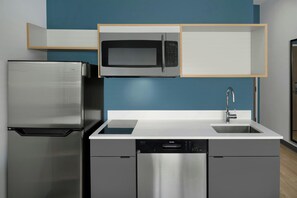 Cocina compacta con refrigerador de acero inoxidable, microondas, lavavajillas y pileta con grifo moderno.