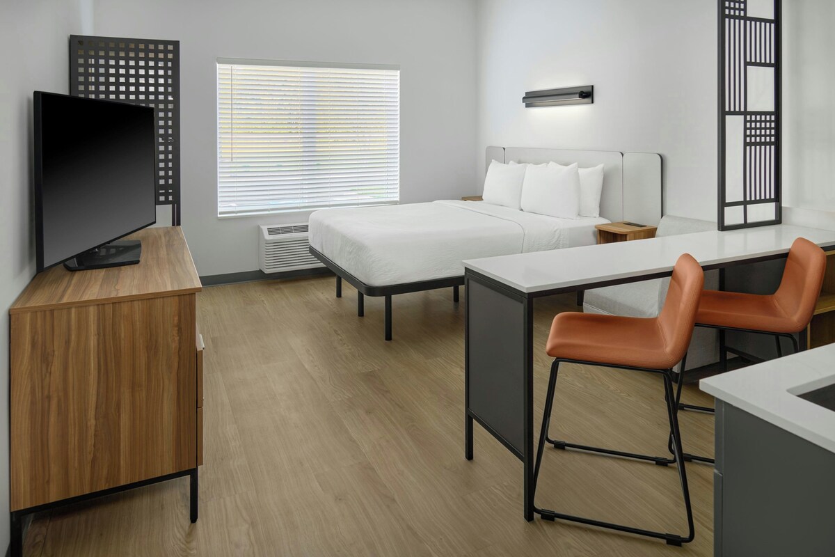A hotel room with a bed, a desk, a chair, a TV, and a window with blinds.