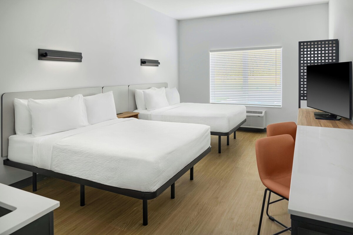 A hotel room with two beds, a TV, and a desk with a chair.