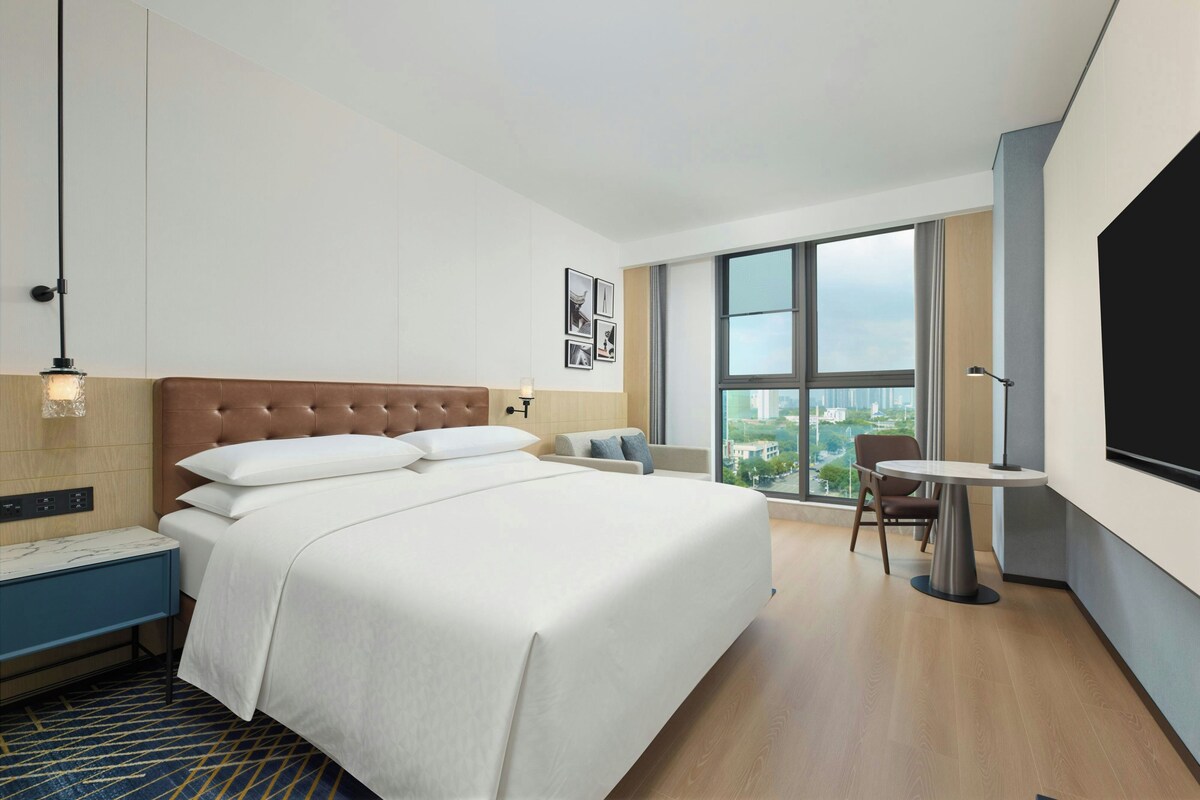 A modern hotel room with a large bed, a desk, and a view of the city.
