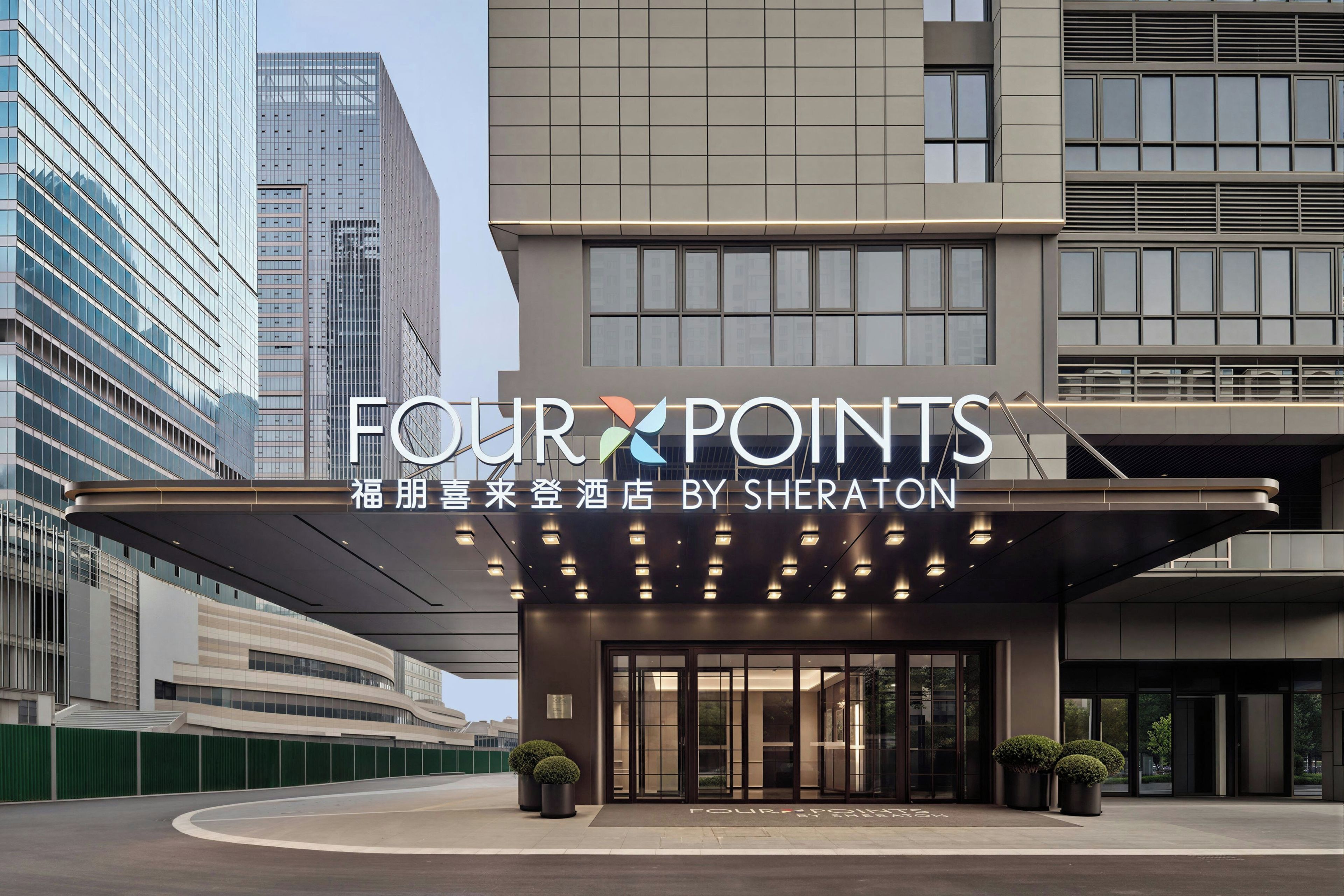 A hotel entrance with a modern design, featuring a large sign that reads 'FOUR POINTS BY SHERATON'.