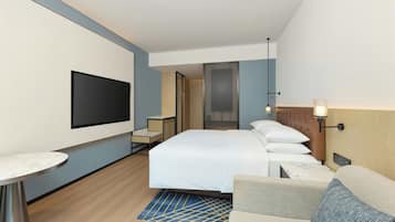 Habitación de hotel con cama, televisión montada en la pared, una mesita y zona de estar con sofá.