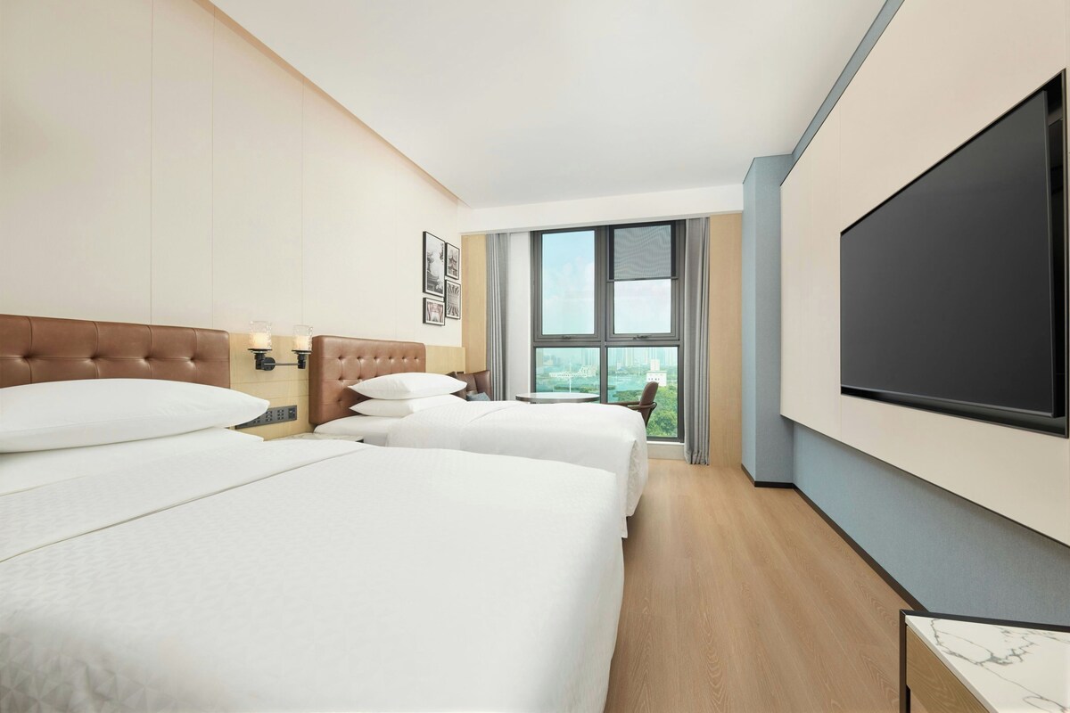A hotel room with two beds, a large TV, and a view of the city.