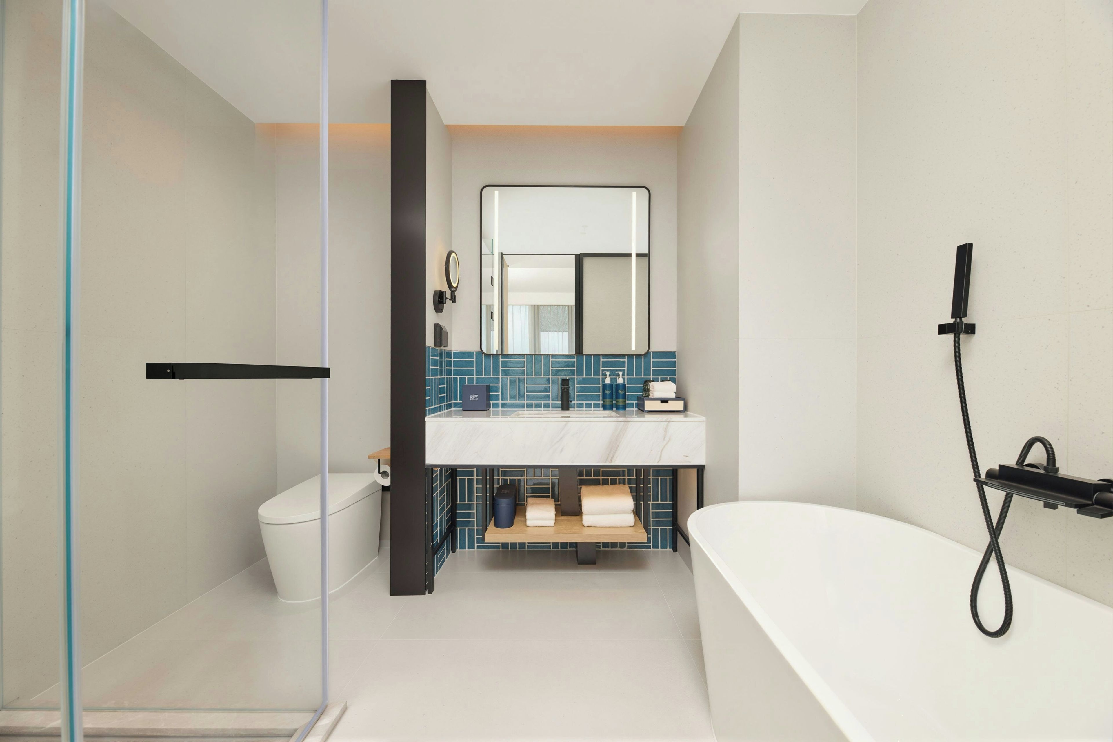 A modern bathroom with a glass shower enclosure, a white toilet, a blue-tiled sink area, and a black handheld showerhead.