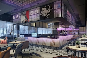 Uma área de bar moderna com cardápio de sushi, placa de check-in/out e letreiro de neon.