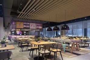 Un interior de restaurante moderno con varias mesas y sillas, una zona de bar y grandes ventanales con vistas a árboles.