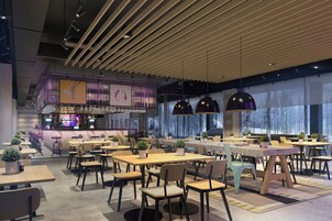 Interior moderno de restaurante com várias mesas e cadeiras, área de bar e janelas amplas com vista para árvores.