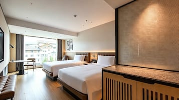Habitació d'hotel amb dos llits, escriptori, cadira i finestra gran que ofereix vistes a edificis.