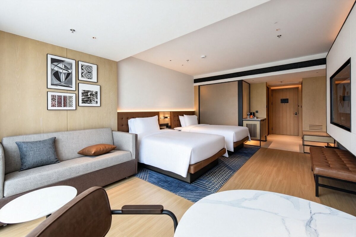 A hotel room with a sofa, two beds, a desk, and a TV.