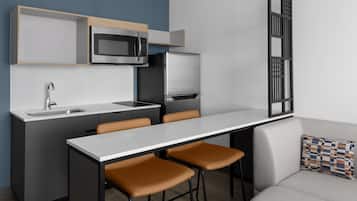 A modern kitchen with a built-in microwave, refrigerator, and sink. There are two bar stools and a dining table.