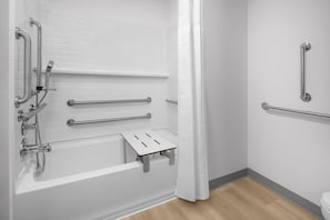 Un baño con una bañera blanca, barras de apoyo y zona de ducha.