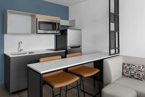 Una cocina moderna con microondas integrado, refrigerador y lavaplatos. Hay un comedor con mesa y sillas.