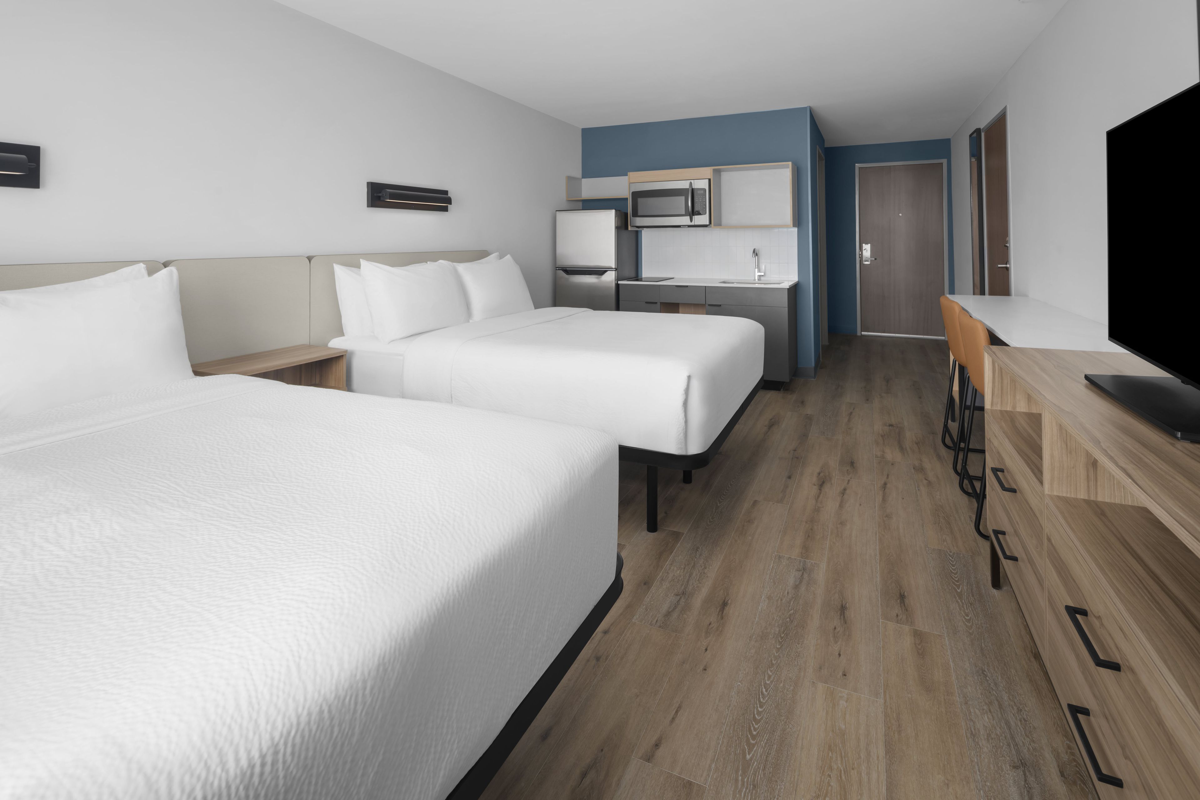 A hotel room with two beds, a kitchenette, a TV, and a wooden floor.