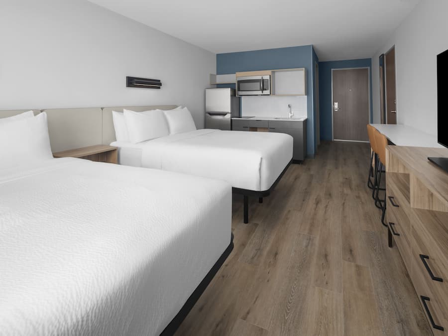 Ein Hotelzimmer mit zwei Betten, einer Küchenzeile, einem Fernseher und Holzboden.