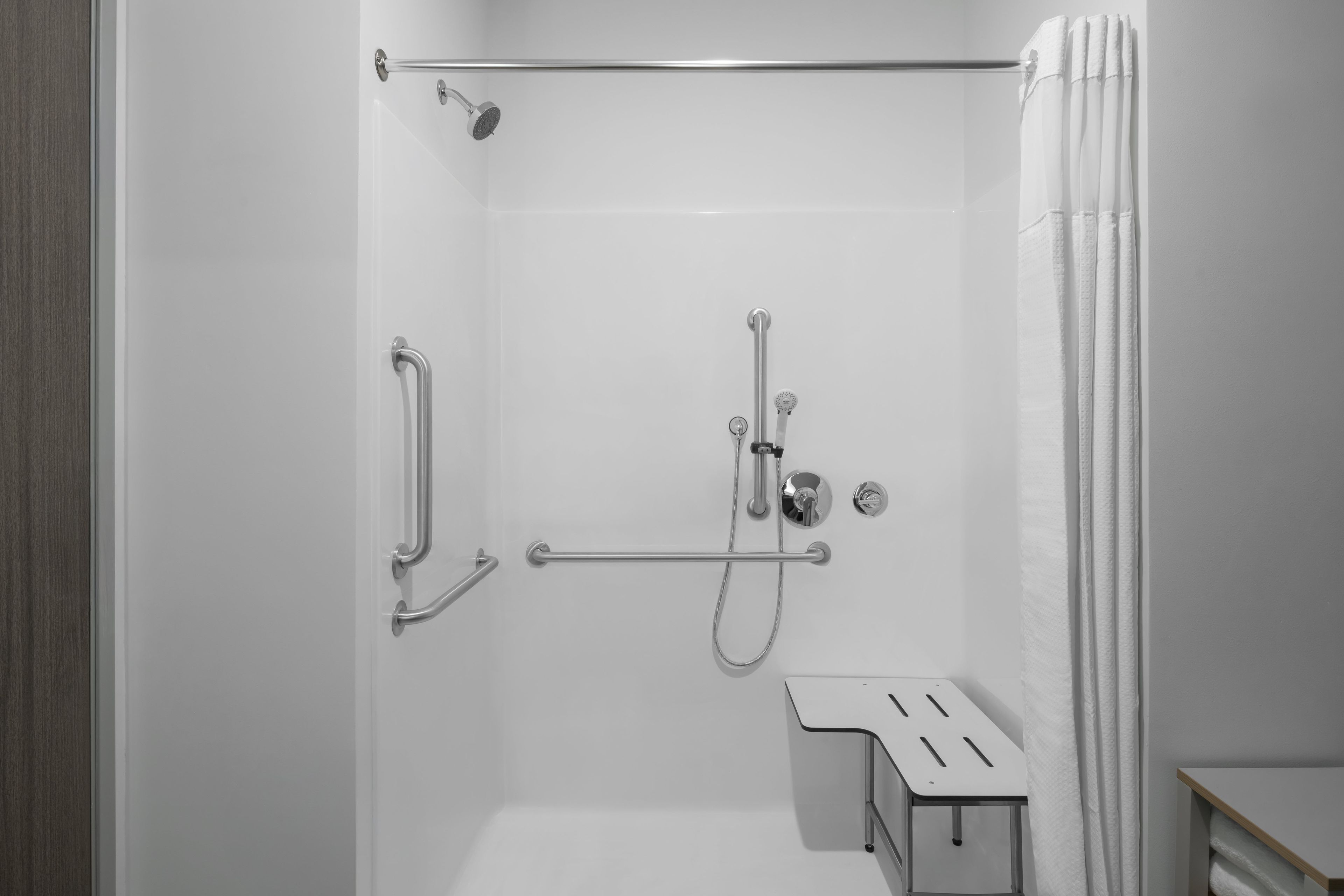 A modern shower area with a glass door, a handheld showerhead, a handheld showerhead, and a grab bar.