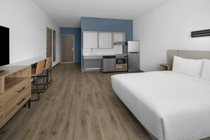 Una habitación de hotel con cama, televisión, escritorio con silla, kitchenette y baño.