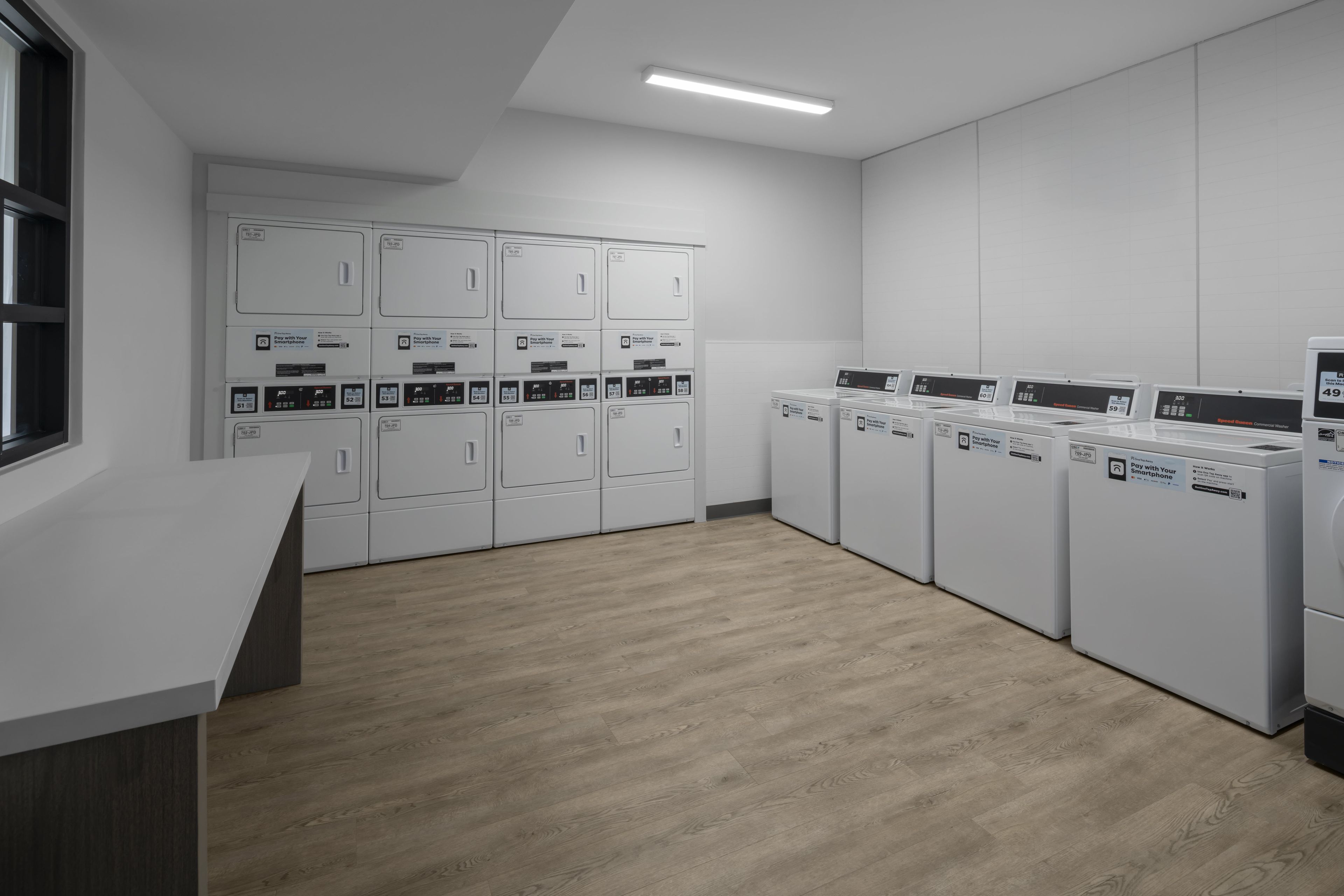 A laundry facility with multiple washing machines and dryers, a white counter, and a wooden floor.