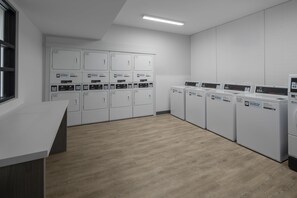 A laundry facility with multiple washing machines and dryers, a white counter, and a wooden floor.