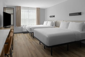 Habitación de hotel con dos camas, un escritorio, un televisor y una ventana con cortinas.