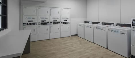 A laundry facility with multiple washing machines and dryers, a white counter, and a window.