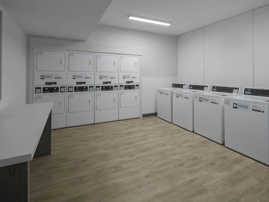 A laundry facility with multiple washing machines and dryers, a white counter, and a window.