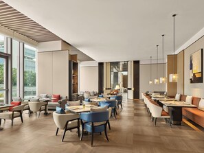 Un restaurant moderne doté de hauts plafonds, de grandes fenêtres et offrant différents types de sièges, notamment des tables et des banquettes.