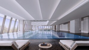 Una piscina interior moderna con paredes de vidrio transparente, sillones de descanso y vistas al exterior.