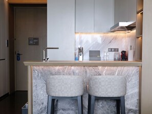 A modern kitchen with a marble countertop, two bar stools, and a built-in range hood.
