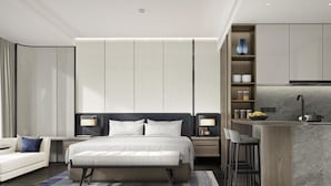 Una habitación de hotel moderna con una cama grande, una zona de estar con sofá, un pequeño espacio de cocina con barra y un baño con ducha.