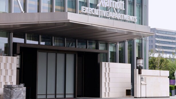 Entrada a un edificio de Marriott Executive Apartments con fachada de vidrio moderna y un área de acceso cubierta.