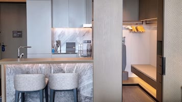 A modern hotel room with a marble bar, two bar stools, a bed, and a built-in wardrobe with hanging clothes.