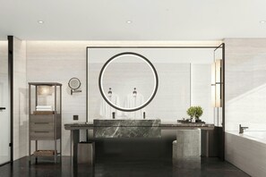 A modern bathroom with a large round mirror, a marble sink, and a small plant.
