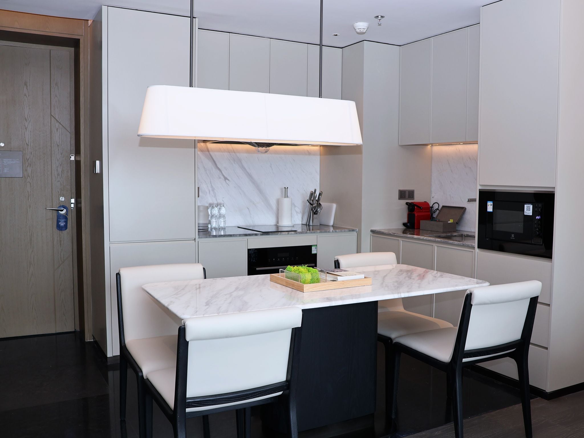 A modern kitchen with a marble countertop, two white chairs, a built-in oven, and a microwave.