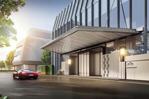 L’entrée d’un hôtel moderne, avec une allée couverte, une voiture garée devant et un bâtiment doté de grandes fenêtres et d’une façade aux lignes géométriques.