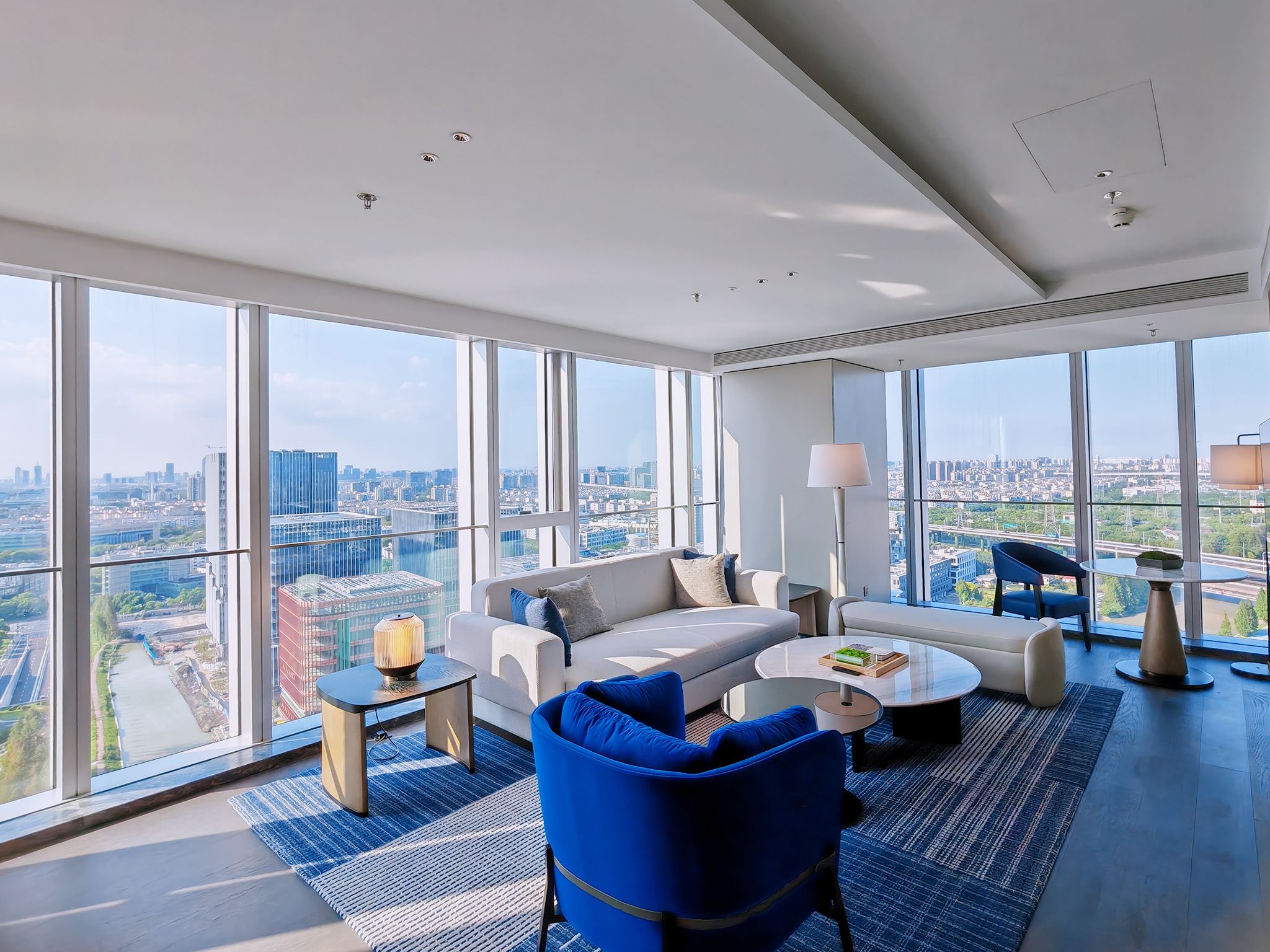 A modern living room with a city view, a sofa, a coffee table, and a blue armchair.