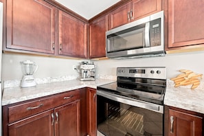 A kitchen with wooden cabinets, a built-in microwave, a stove, an oven, and a coffee maker. - Oceanview Pool Beach Stay @Villa Capriani 3 Kings (North Topsail Beach)