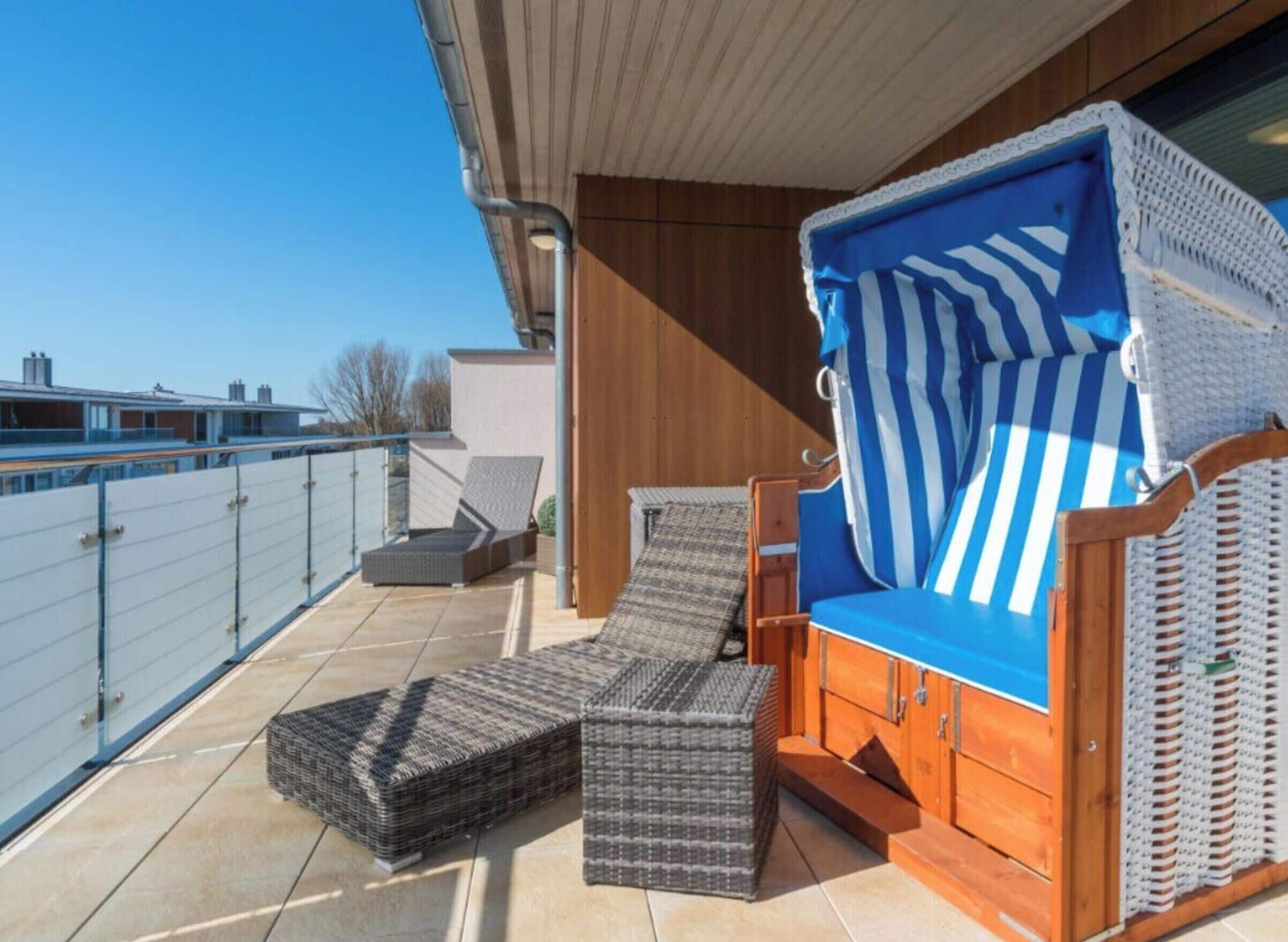 A balcony with wicker furniture, a blue-striped cushion, and a wooden cabinet.