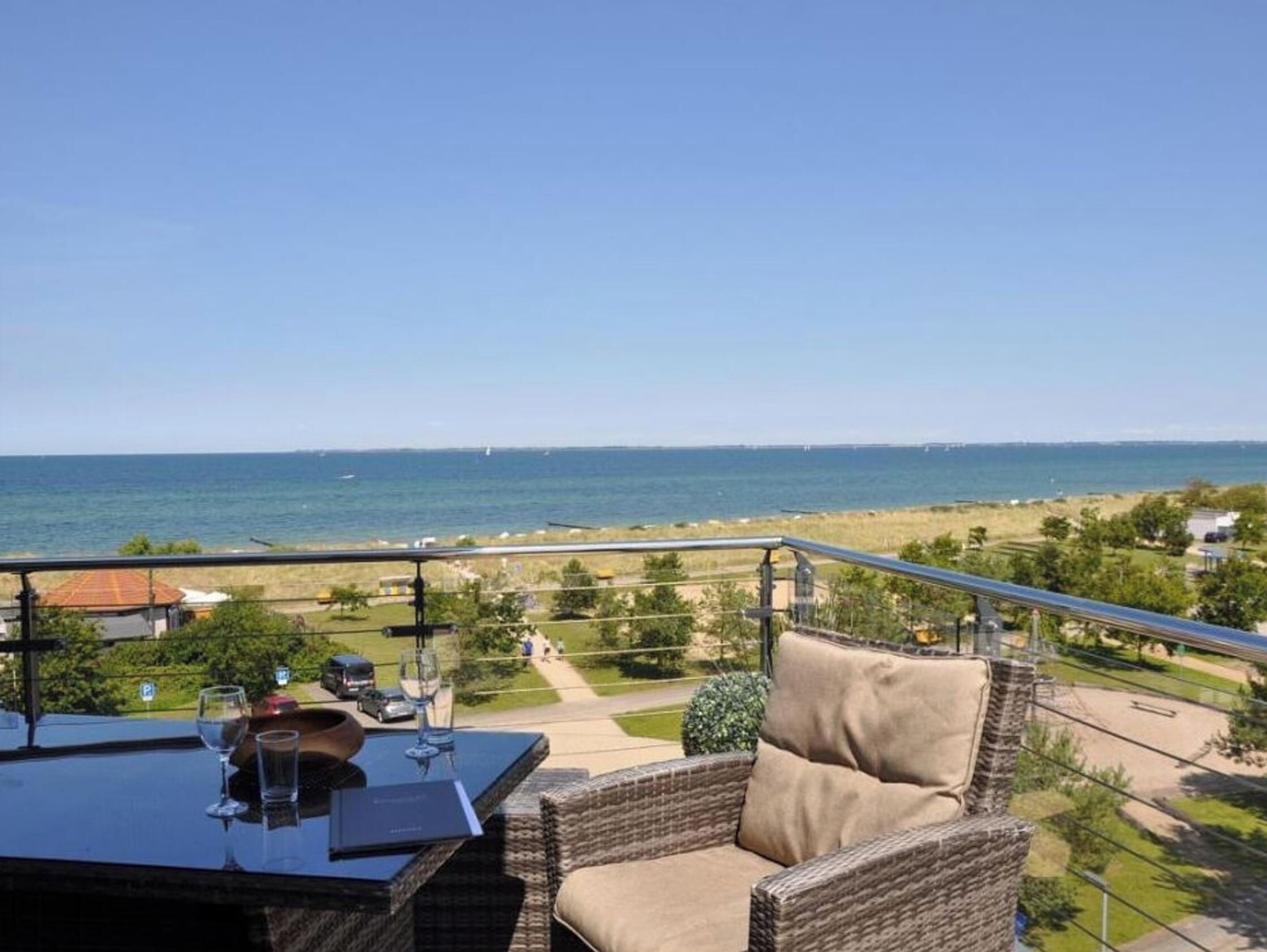A balcony with wicker furniture, a glass table, and a view of the sea.