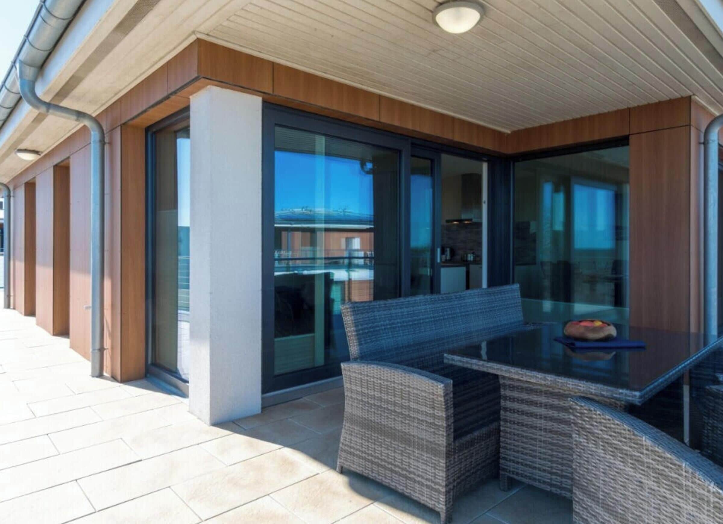 A covered outdoor seating area with a table and chairs, a glass door leading to a kitchen, and a tiled floor.