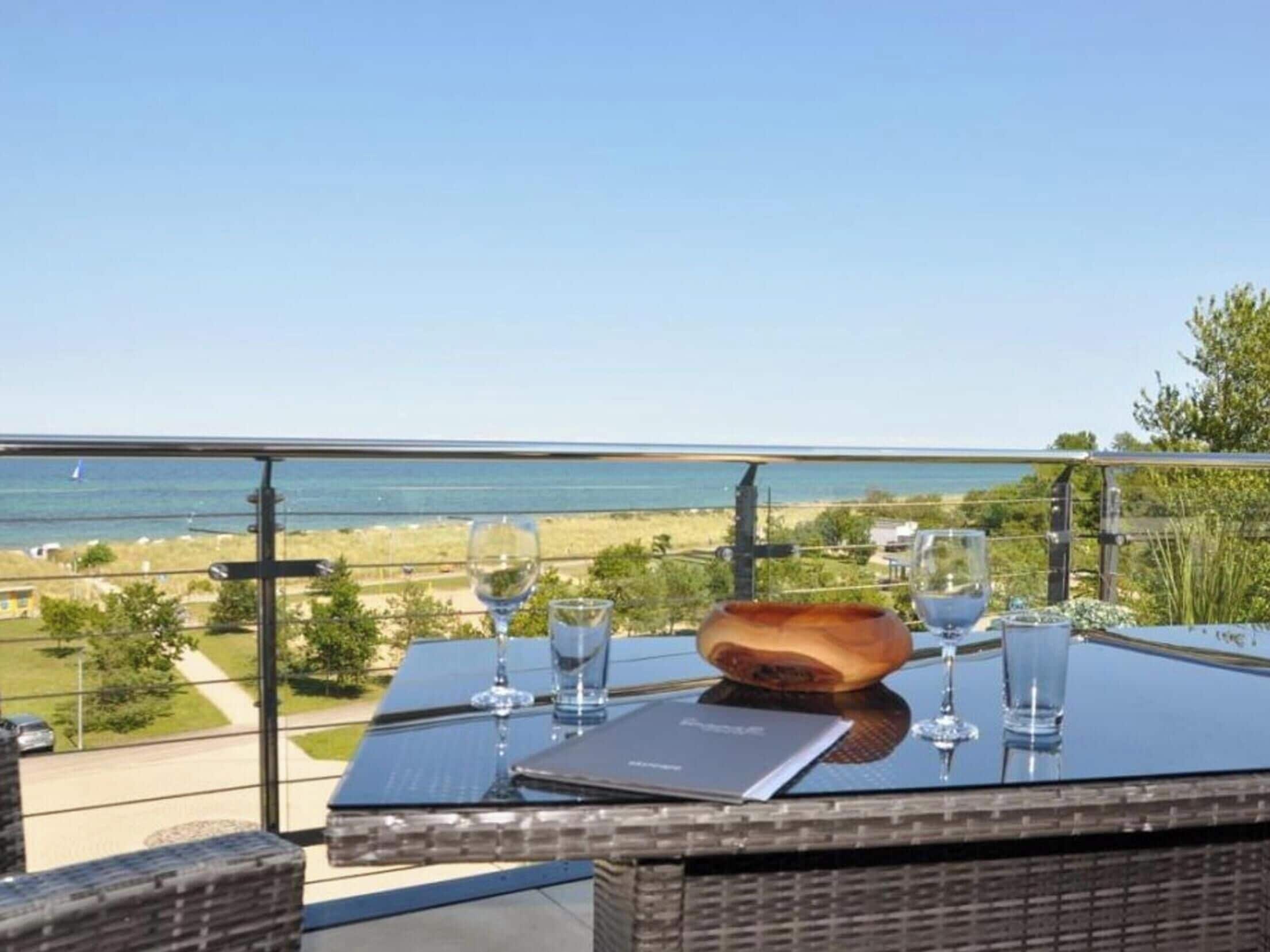 Ein Tisch mit Blick auf Strand und Meer, ein Glas Wasser und eine Holzschüssel.