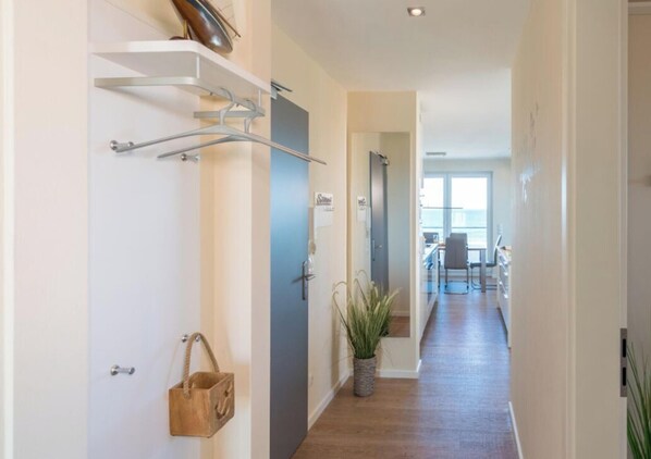 Un couloir avec un porte-manteau, une porte, une plante et une vue sur un coin repas.