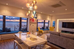 A modern living room with a dining area, large windows with a view of the sea, and a flat-screen TV mounted on the wall. - The Hideaway | Stunning Sea Views & Stylish Stay (Vale of Glamorgan)