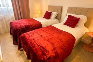 A hotel room with two beds, each with a red bedspread and white pillows. There is a small bedside table with a lamp on it. - The Hideaway | Stunning Sea Views & Stylish Stay (Vale of Glamorgan)